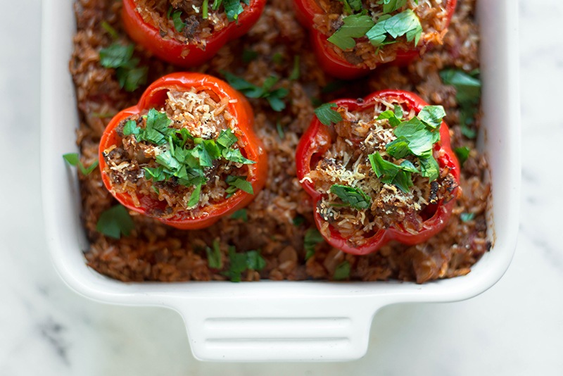 Partial overhead view of a casserole dish with baked classic stuffed peppers, stuffed with rice and ground beef, and topped with fresh italian parsley.