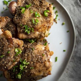 close up photo of crispy chicken thighs on a plate with diced chilies on top