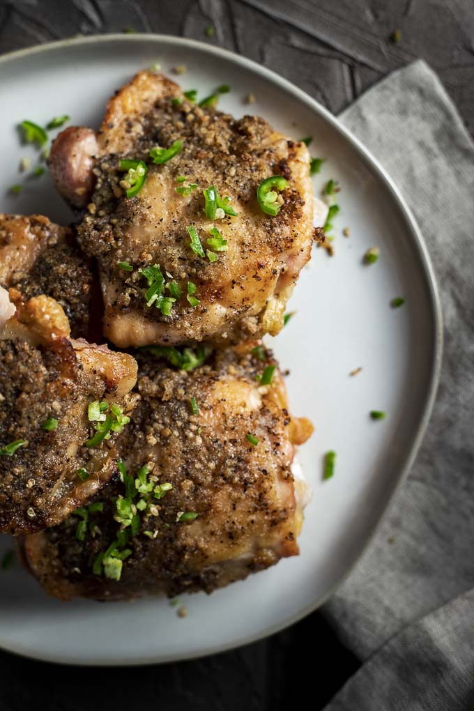 close up photo of crispy chicken thighs on a plate with diced chilies on top